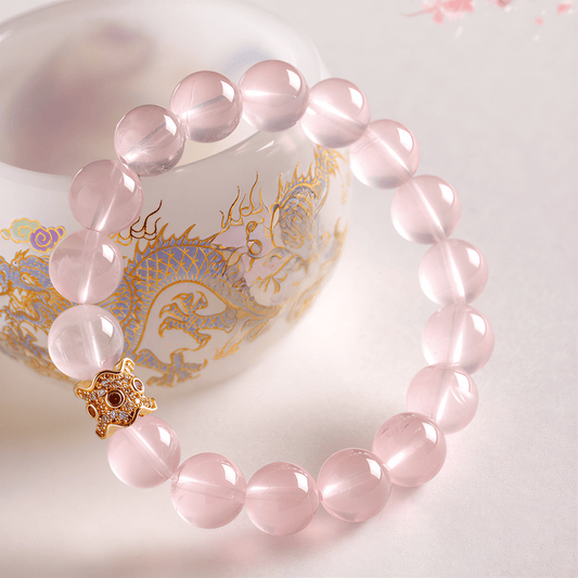 Detailed view of My Heart Is Safe Rose Quartz bracelet with gold-tone charm beside decorative porcelain cup