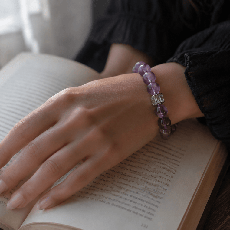 Woman wearing A Clear Way Through Amethyst bracelet while reading a book