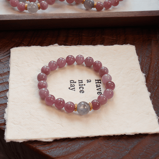 Held by the Moon Purple Mica Rose Quartz bracelet displayed on soft cloth with Gray Moonstone centerpiece