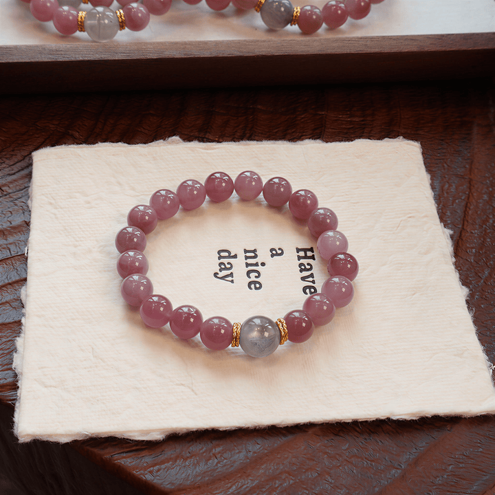 Held by the Moon Purple Mica Rose Quartz bracelet displayed on soft cloth with Gray Moonstone centerpiece