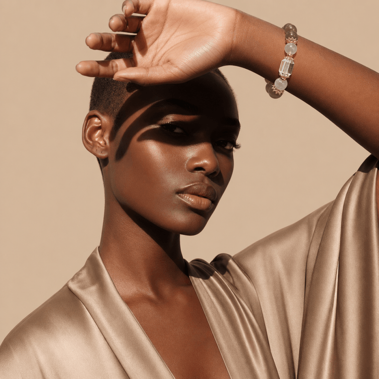 Model wearing Gray Moonstone and Clear Quartz bracelet with gold-tone accents and satin robe in warm sunlight