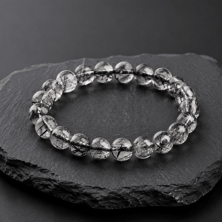 I Am Protected Black Rutilated Quartz bracelet worn with black sleeve beside a gray concrete wall