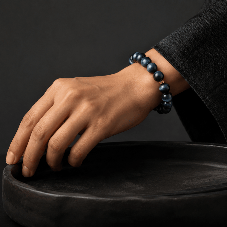 Blue Tiger's Eye bracelet worn on wrist beside a black ceramic bowl in a dark minimal setting