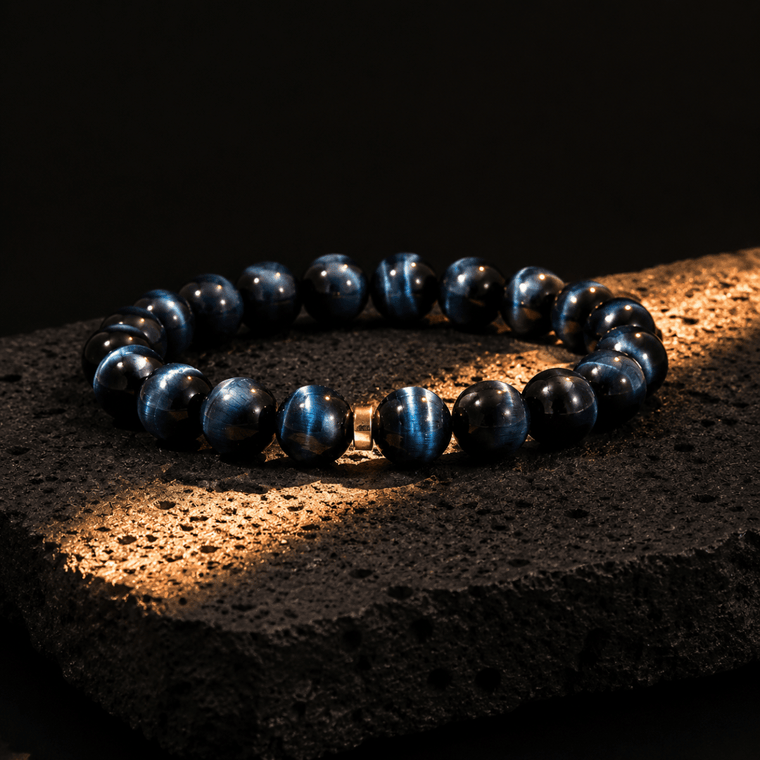 Natural Blue Tiger's Eye bracelet displayed on black volcanic stone under warm light