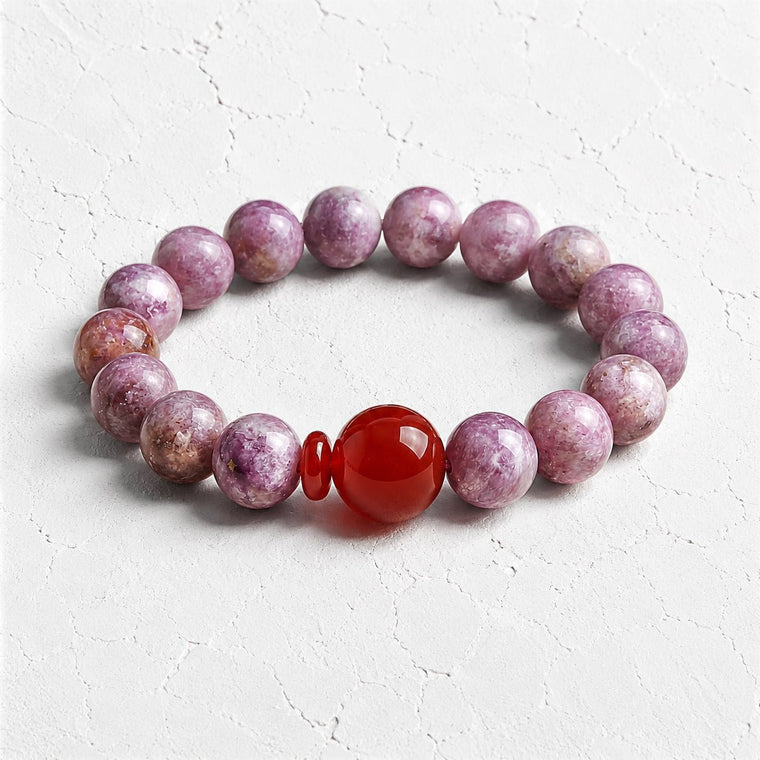 Flat lay of I Trust My Fire bracelet with lilac Amethyst beads and a red center accent on a white textured surface