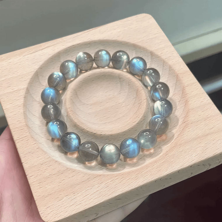 Close-up of Blue Flash Gray Moonstone bracelet displayed on a wooden tray in natural light