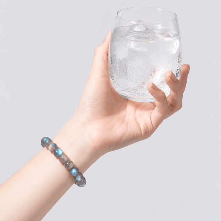 Blue Flash Gray Moonstone bracelet worn on wrist while holding a clear glass of water