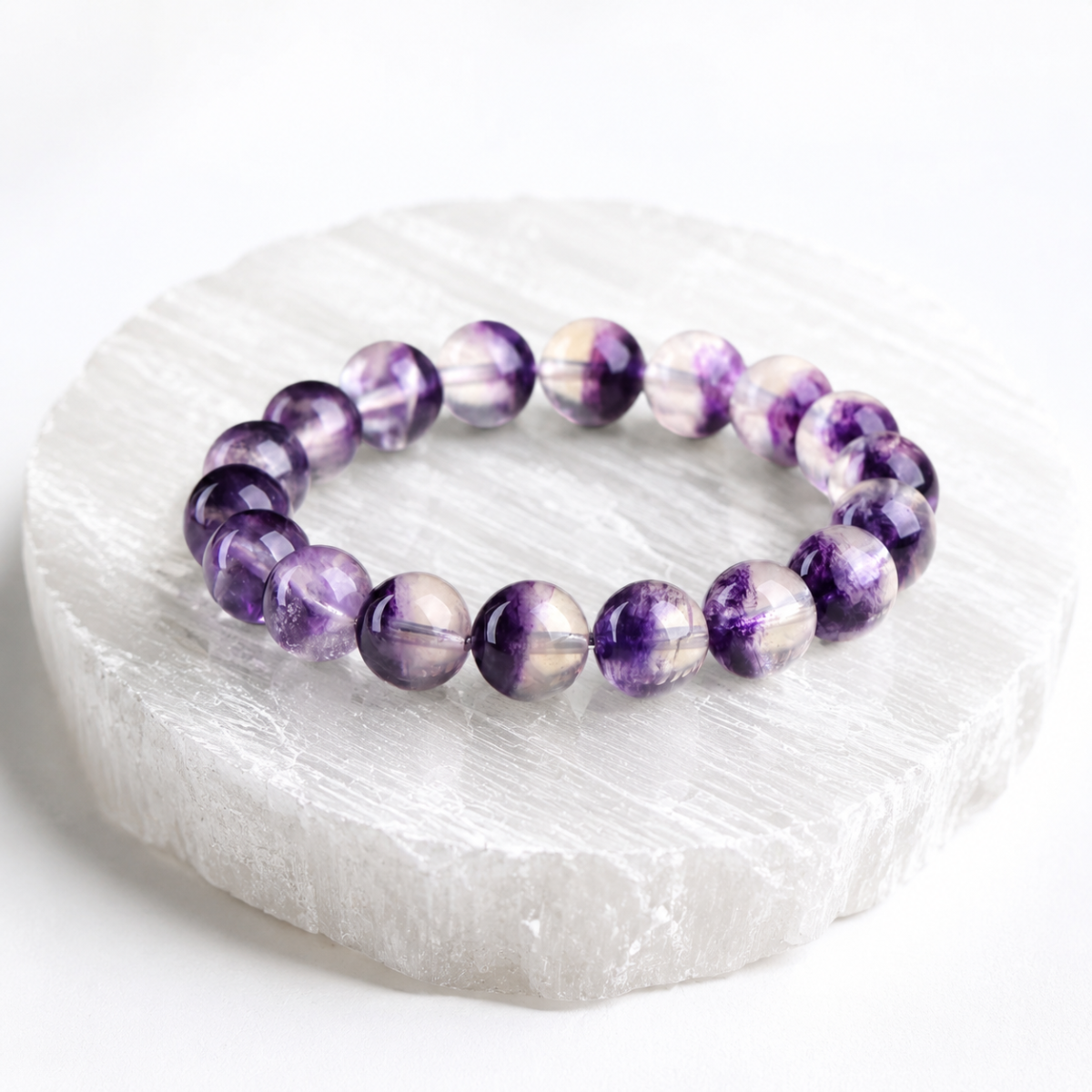 Amethyst crystal bracelet resting on a white selenite plate for cleansing and recharging