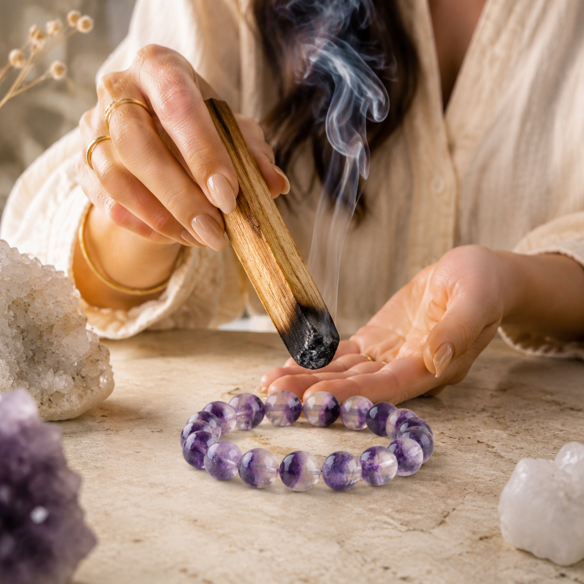 Hands using palo santo smoke to cleanse an amethyst crystal bracelet