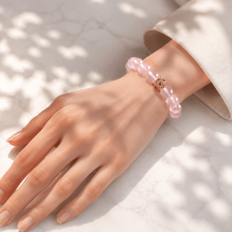 Woman wearing My Heart Is Safe Rose Quartz bracelet with gold-tone charm in soft natural sunlight