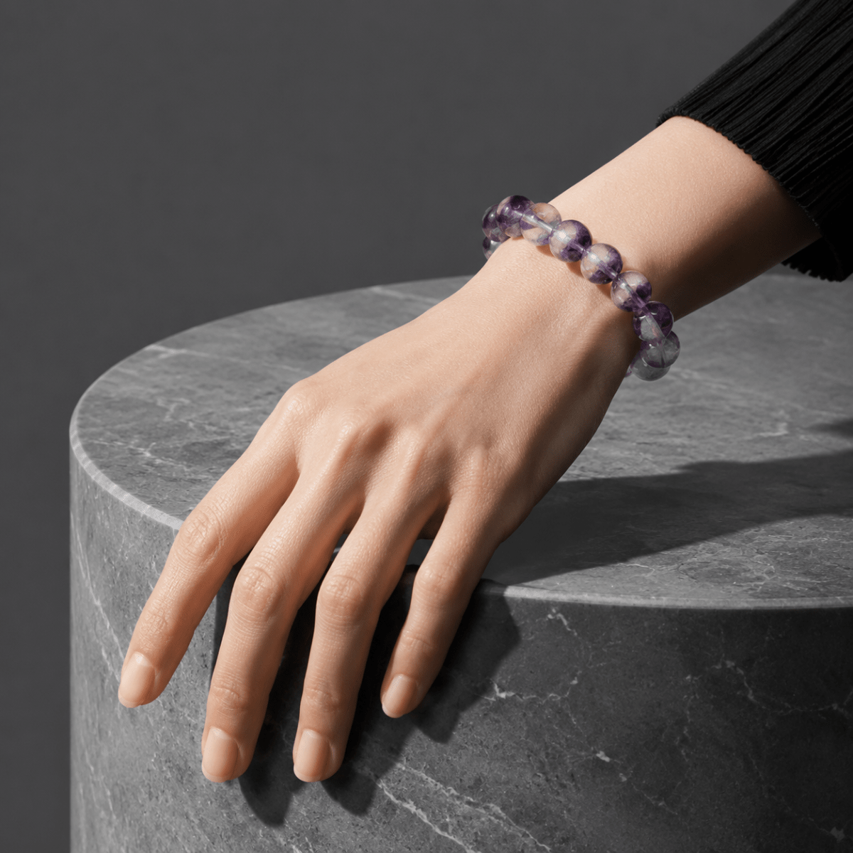 Purple Fluorite bracelet worn with a black sleeve beside a dark stone surface