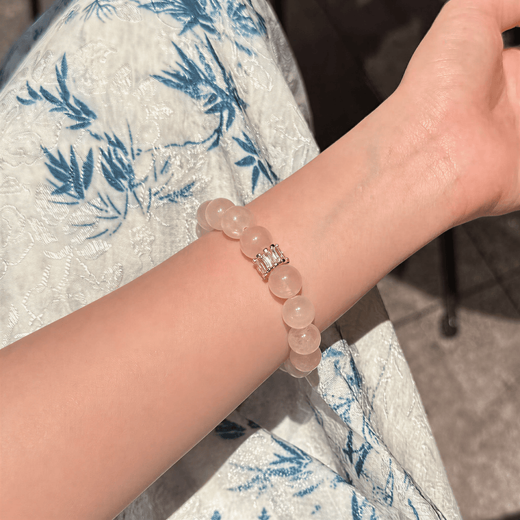 Rose Quartz bracelet with gold-tone centerpiece worn on the wrist in natural sunlight