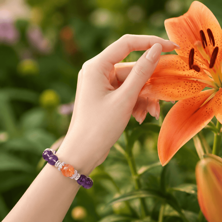 Woman wearing The Courage to Bloom Amethyst bracelet beside an orange flower