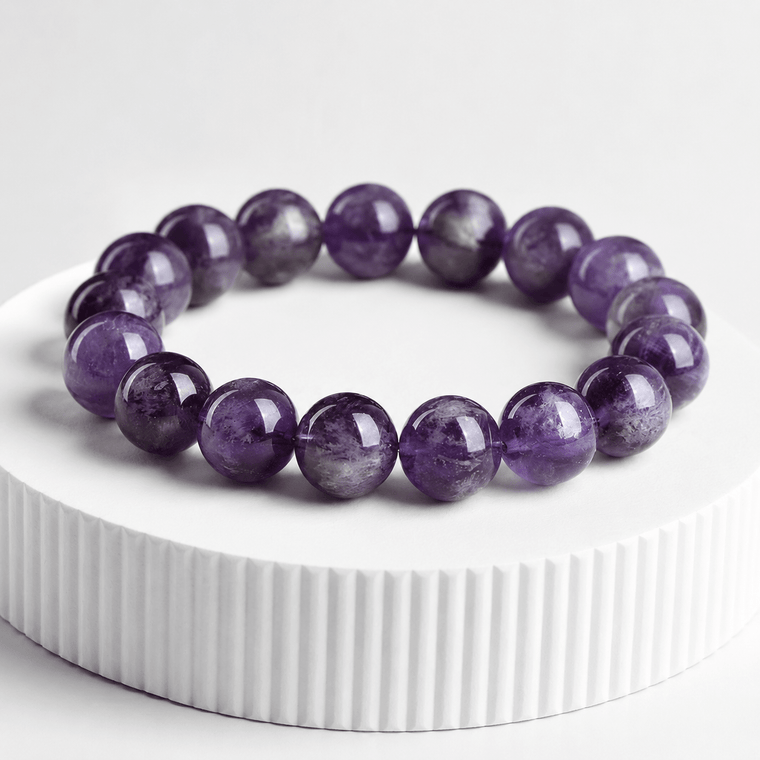 The Stillness Within Amethyst bracelet displayed on a white pedestal with deep purple 12mm beads