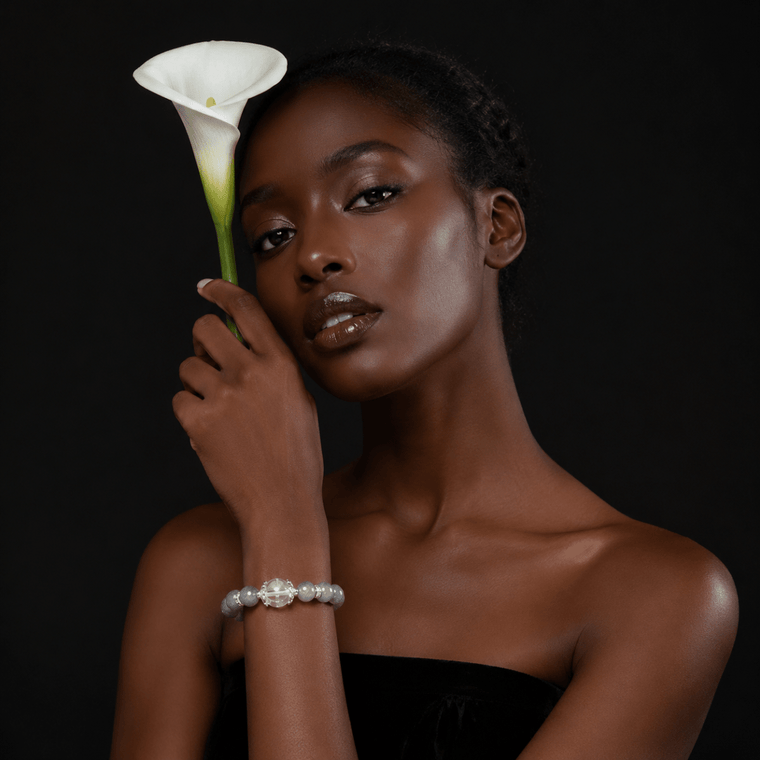 Model wearing Moonstone and Clear Quartz bracelet while holding a white calla lily against a dark background
